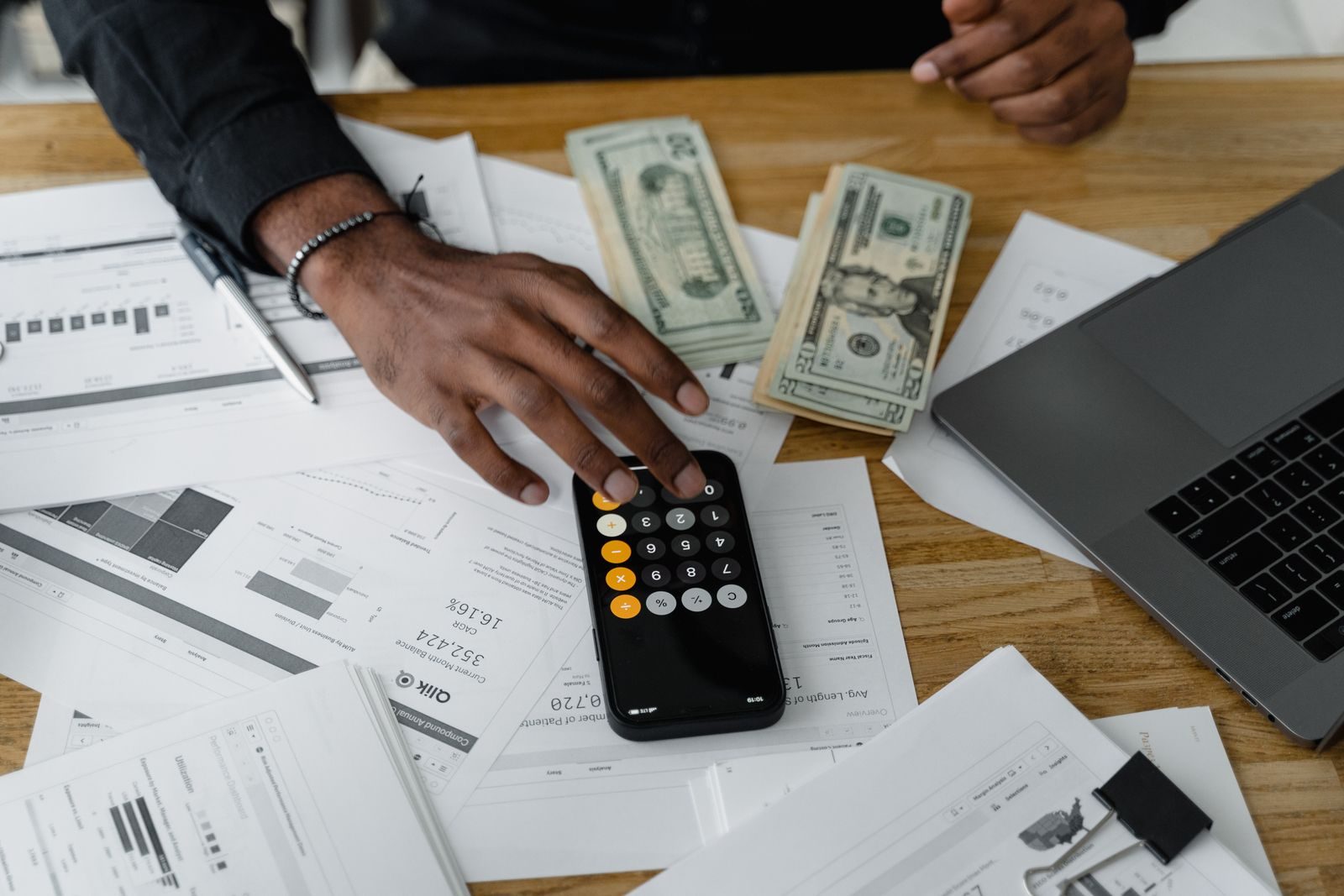 A laptop on a desk beside cash and paperwork